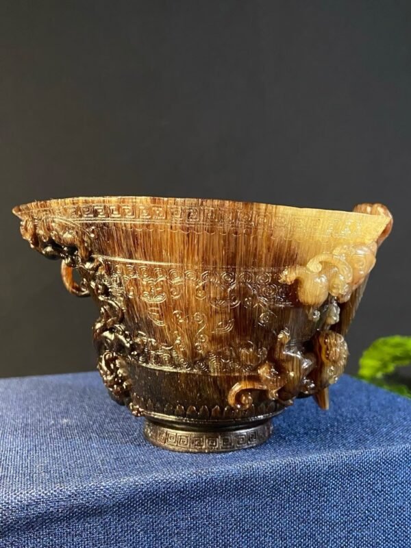 Carved natural horn relief cup with dragon-head finial on the rim, displayed on blue cloth